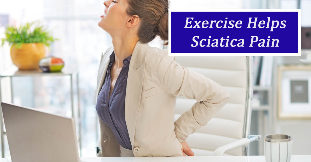 Exercises for Sciatica. Picture of a young caucasian female sitting at a desk and holding her lower back as if in pain.